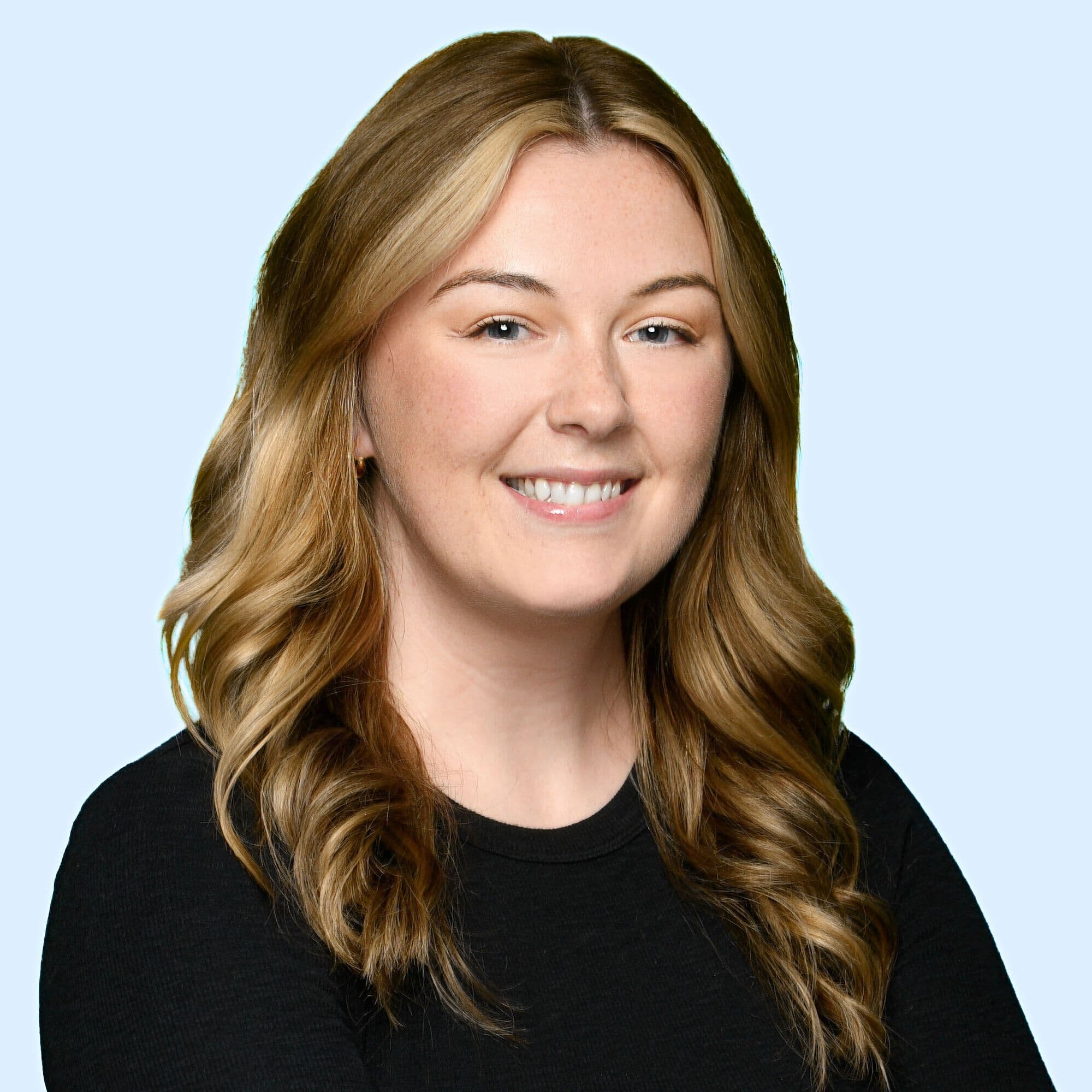 Image 7: Professional headshot of Madisyn MacMillan, smiling with wavy highlighted hair on blue background